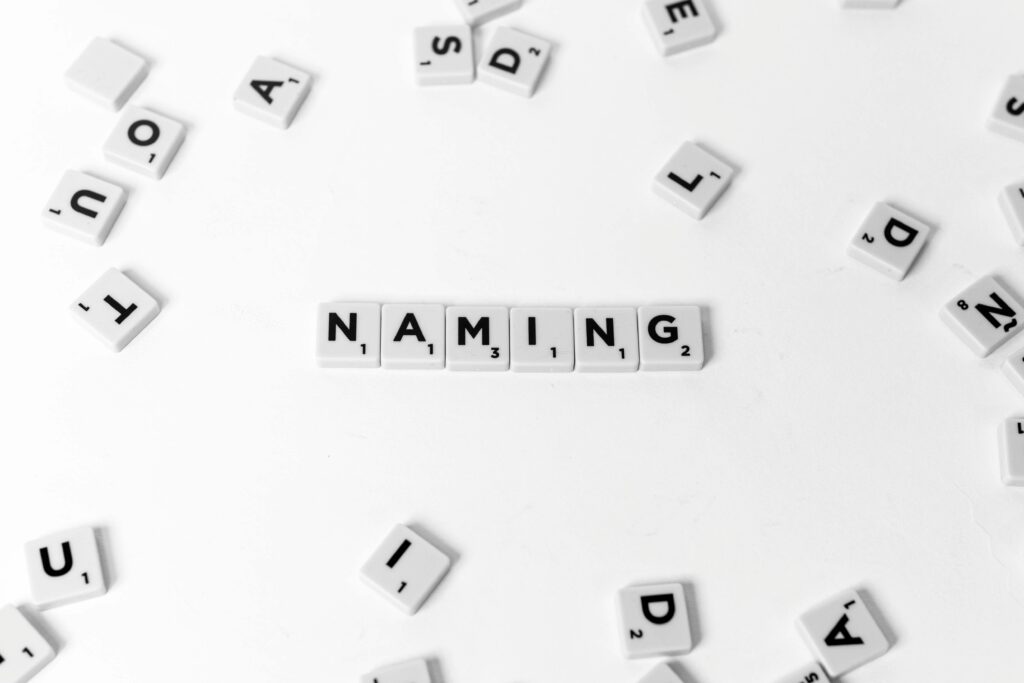 Flat lay of scattered Scrabble tiles spelling 'NAMING' on a white background.